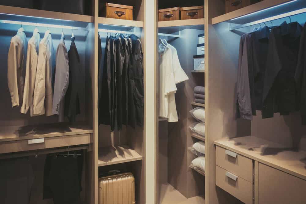 A lit walk-in closet with hanging rails, shelving, and drawers