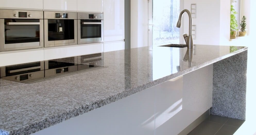 A stone worktop running past a sink and built-in ovens