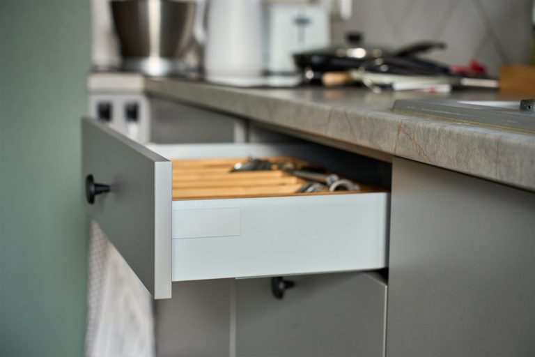Pull-out kitchen drawer with a wooden utensil organizer under a stone countertop