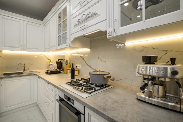 Under-cabinet LED strip lighting over a gray countertop and cooktop in a white kitchen