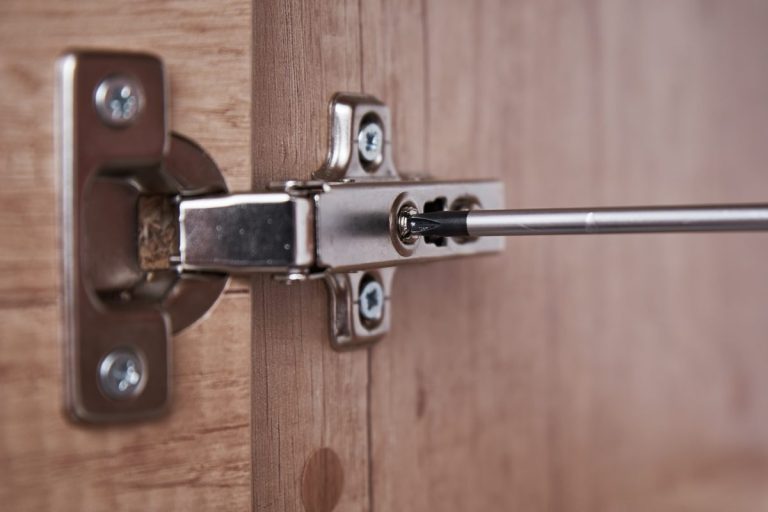 Screwdriver adjusting a concealed hinge on a wooden cabinet door